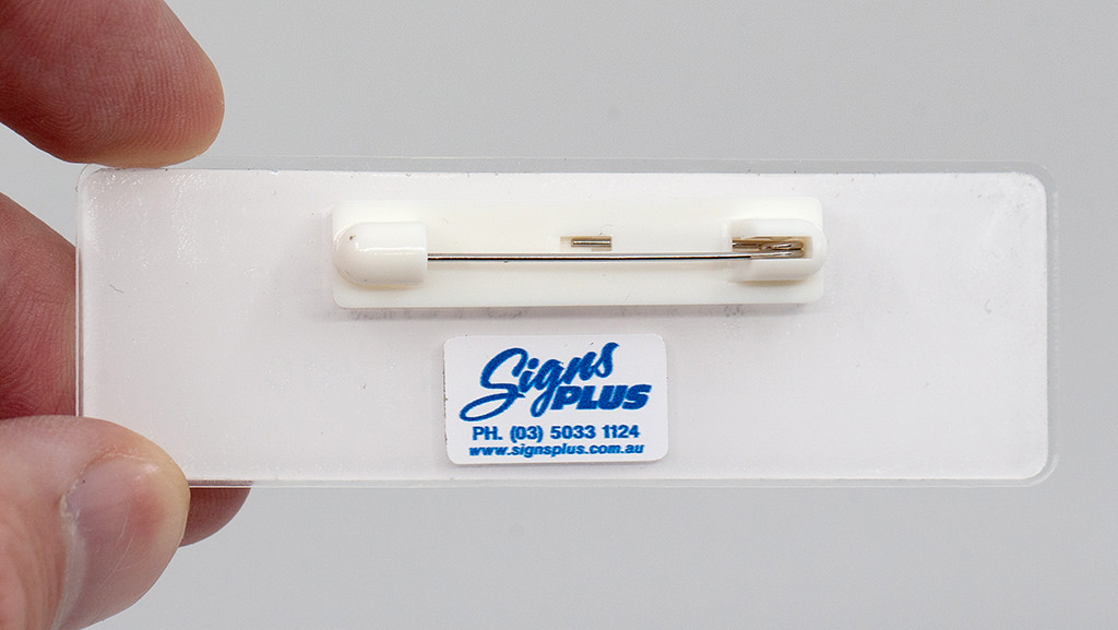Close-up of name badge showing traditional pin attachment mechanism on back with Signs Plus branding